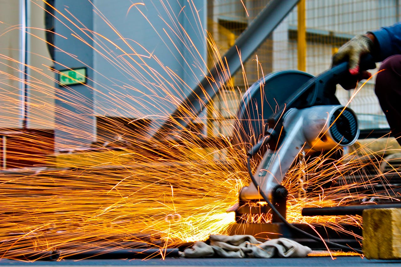 project-01-c A worker operates a grinder cutting metal, creating a vibrant display of sparks in an industrial setting.