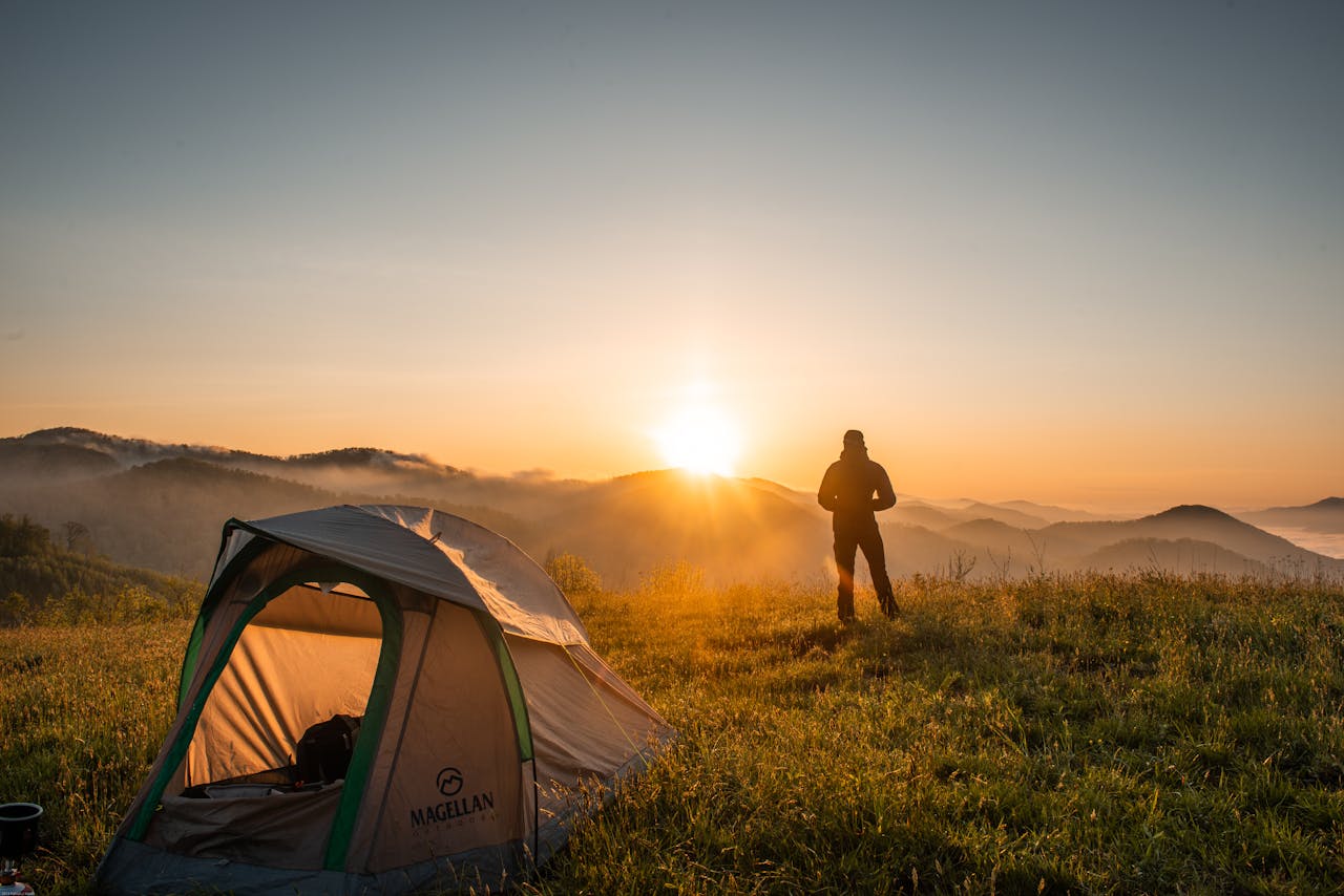 contact-header A camper enjoys the sunrise in a mountain setting with a tent. Perfect nature escape.