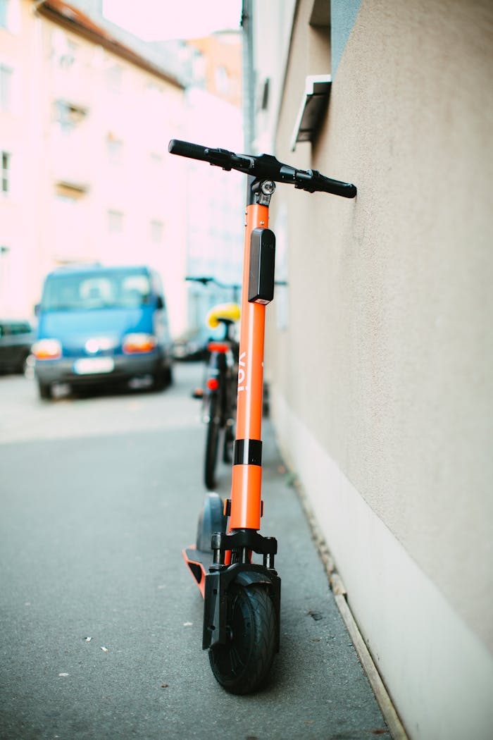 about-04 Vibrant orange electric scooter parked on a city sidewalk during daylight, showcasing urban transportation.