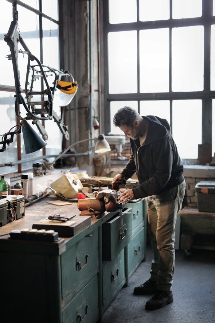 project-01-d Side view of bearded male master in casual clothes standing at workbench and fixing details with professional metal instrument