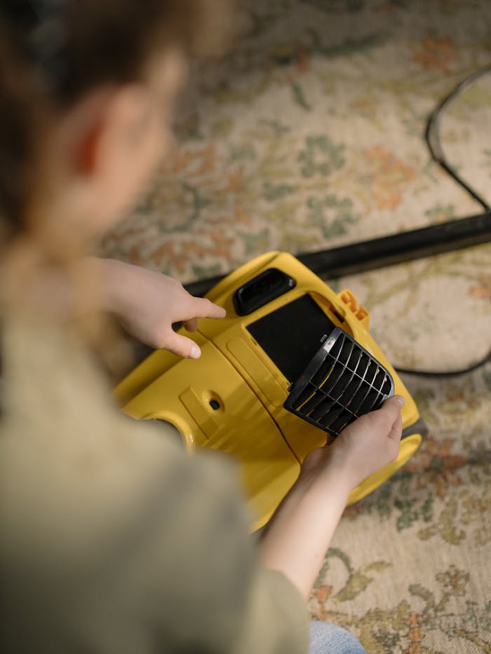project-03-d A person cleans and maintains a yellow vacuum cleaner on a patterned carpet indoors.