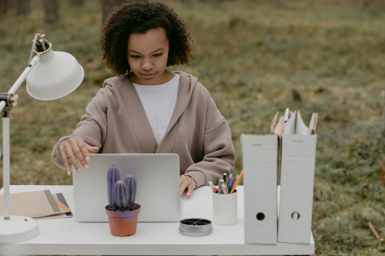 project-01-b Focused young woman working on laptop outdoors. Remote work setup with nature background.
